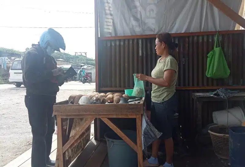 Seorang pedagang sedang melayani pembeli buah kelapa di salah satu tempat jual kelapa tua di Jalan Raya Pasar Youtefa, Kota Jayapura, Papua pada Rabu (19/03/2025). Jubi/Aida Ulim.